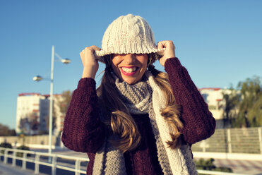 Spain, Cadiz, El Puerto de Santa Maria, playful woman covering her face with wooly hat - KIJF000038