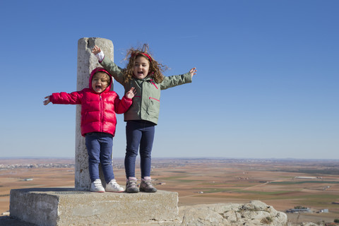 Spain, Consuegra, two happy little girls standing on summit with arms outstretched stock photo