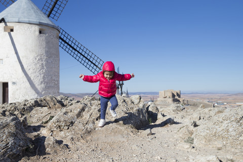 Spain, Consuegra, jumping little girl with windmill in the background stock photo