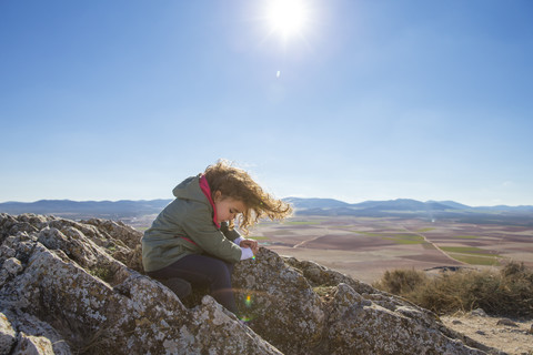 Spanien, Consuegra, kleines Mädchen sitzt auf einem Felsen eines Berges, lizenzfreies Stockfoto