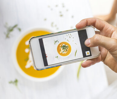 Frau fotografiert mit ihrem Smartphone eine Karotten-Kürbissuppe, Nahaufnahme - KNTF000210