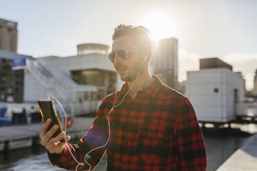 Ireland, Dublin, young man at city dock listening to music - BOYF000050