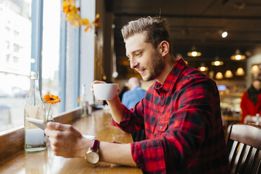 Mann in einem Café mit Blick auf eine digitale Tafel - BOYF000054
