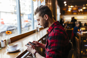 Mann in einem Café schaut auf sein Handy - BOYF000055