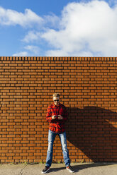 Junger Mann an einer Backsteinmauer, der ein Mobiltelefon benutzt - BOYF000062
