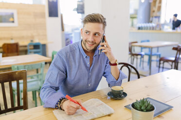 Mann mit Zeitung, der in einem Café sitzt und mit seinem Smartphone telefoniert - BOYF000074
