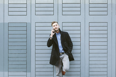 Young businessman leaning against facade telephoning with smartphone - BOYF000077