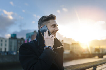 Irland, Dublin, lächelnder junger Geschäftsmann telefoniert mit Smartphone bei Gegenlicht - BOYF000079