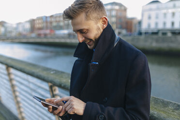 Irland, Dublin, lächelnder junger Geschäftsmann schaut auf sein Smartphone - BOYF000080