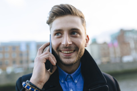 Ireland, Dublin, portrait of smiling young businessman telephoning with smartphone stock photo