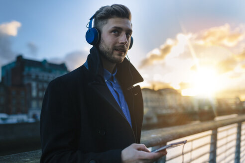 Irland, Dublin, junger Mann, der in der Dämmerung mit Kopfhörern Musik hört - BOYF000086