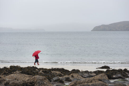 Großbritannien, Schottland, Isle of Skye, Spaziergängerin mit Schirm am verregneten Strand - JBF000254