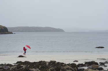 UK, Schottland, Isle of Skye, Spaziergängerin mit Regenschirm am regnerischen und stürmischen Strand - JBF000255