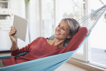 Smiling woman at home lying in hammock looking at digital tablet - RBF003566