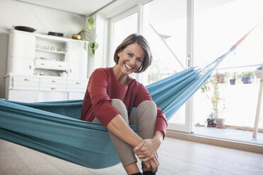 Happy woman at home sitting in hammock - RBF003571