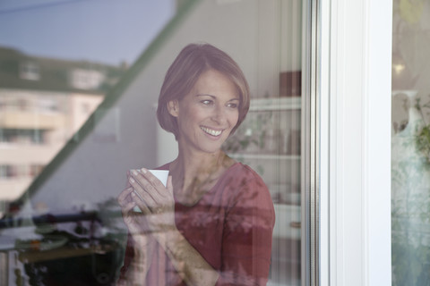 Lächelnde Frau mit Tasse und Blick aus dem Fenster, lizenzfreies Stockfoto