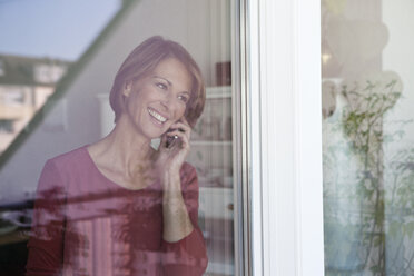 Lächelnde Frau beim Telefonieren am Fenster - RBF003574