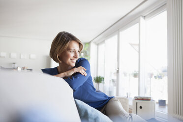 Lächelnde Frau zu Hause auf der Couch sitzend - RBF003575