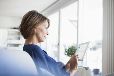 Woman at home sitting on couch using digital tablet - RBF003579