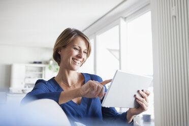 Lächelnde Frau zu Hause auf der Couch sitzend mit digitalem Tablet - RBF003580