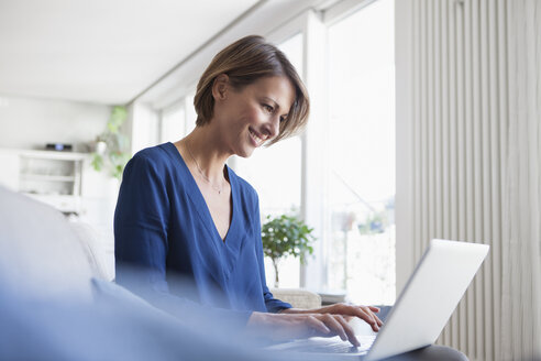 Lächelnde Frau zu Hause auf der Couch sitzend mit Laptop - RBF003582