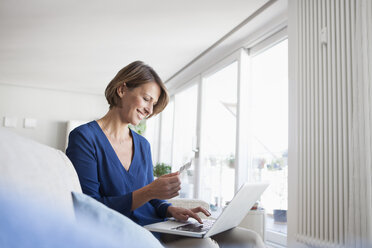 Lächelnde Frau beim Online-Einkauf zu Hause - RBF003585