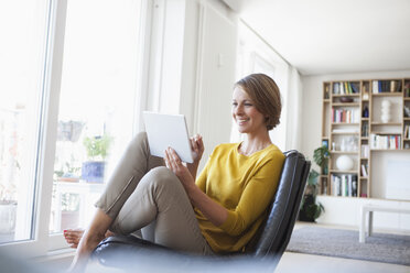 Entspannte Frau, die zu Hause auf einem Ledersessel sitzt und ein digitales Tablet benutzt - RBF003600