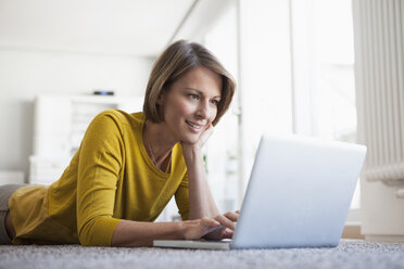 Relaxed woman at home lying on floor using laptop - RBF003610