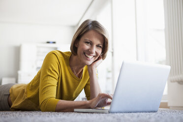 Relaxed woman at home lying on floor using laptop - RBF003611