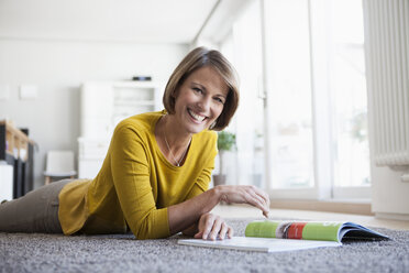 Relaxed woman at home lying on floor reading magazine - RBF003613