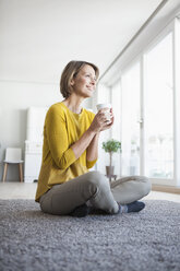 Entspannte Frau zu Hause, die auf dem Boden sitzt und eine Tasse hält - RBF003614
