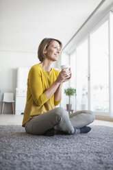 Relaxed woman at home sitting on floor holding cup - RBF003614