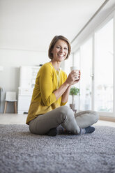 Entspannte Frau zu Hause, die auf dem Boden sitzt und eine Tasse hält - RBF003615
