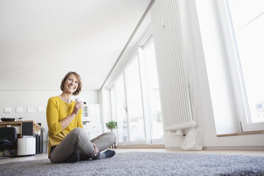 Entspannte Frau zu Hause, die auf dem Boden sitzt und eine Tasse hält - RBF003616