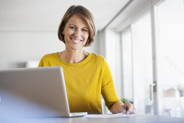 Porträt einer lächelnden Frau zu Hause am Laptop - RBF003623