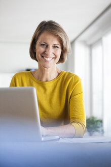 Porträt einer lächelnden Frau zu Hause am Laptop - RBF003624