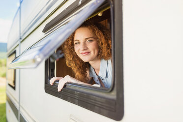 Porträt einer lächelnden jungen Frau, die durch das Fenster eines Wohnwagens schaut - HAPF000040