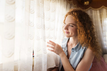 Smiling young woman sitting in a caravan looking through window - HAPF000042