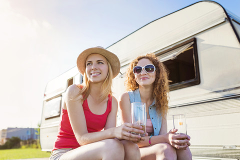 Porträt von zwei Freundinnen, die im Sommer vor einem Wohnwagen sitzen, lizenzfreies Stockfoto