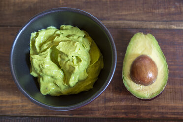 Bowl of guacamole and half of an avocado on wood - SARF002394