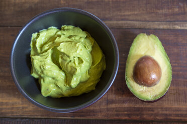 Schale mit Guacamole und einer halben Avocado auf Holz - SARF002394