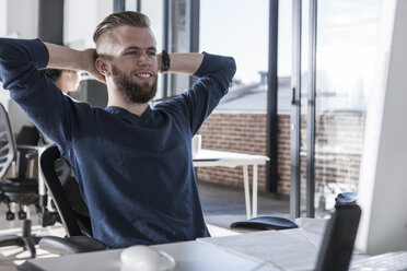 Junger Mann sitzt am Schreibtisch, arbeitet im Büro - ZEF007489