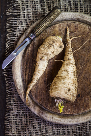 Petersilienwurzeln und Sparschäler auf Holzbrett und Jute, lizenzfreies Stockfoto