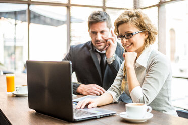 Zwei Geschäftspartner sitzen in einem Café und schauen auf einen Laptop - OIPF000012