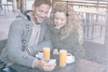 Happy couple sitting in a coffee shop looking at smartphone - OIPF000020