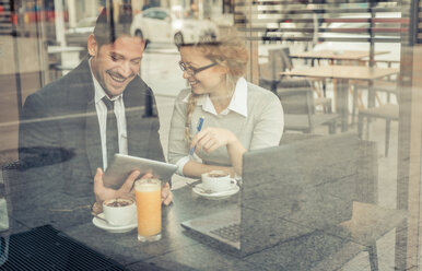 Zwei lächelnde Geschäftspartner sitzen in einem Café mit digitalem Tablet und Laptop - OIPF000021