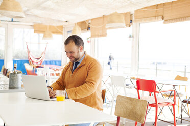 Spain, Barcelona, smiling businessman sitting at seaside cafe using laptop - VABF000007