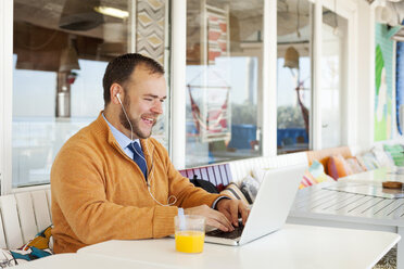 Spain, Barcelona, smiling businessman sitting at seaside cafe using laptop - VABF000008