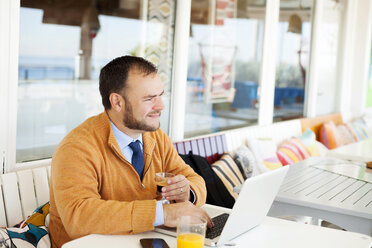 Spanien, Barcelona, lächelnder Geschäftsmann in einem Café am Meer mit Laptop und einer Tasse Espresso - VABF000009