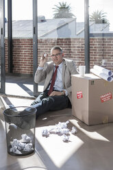 Businessman sitting on the floor in a new office throwing crumpled paper - ZEF007547